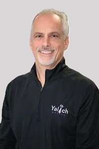 Smiling middle-aged man with short gray hair and a goatee wearing a black pullover with a “Valtech” logo, standing in front of a plain gray background.